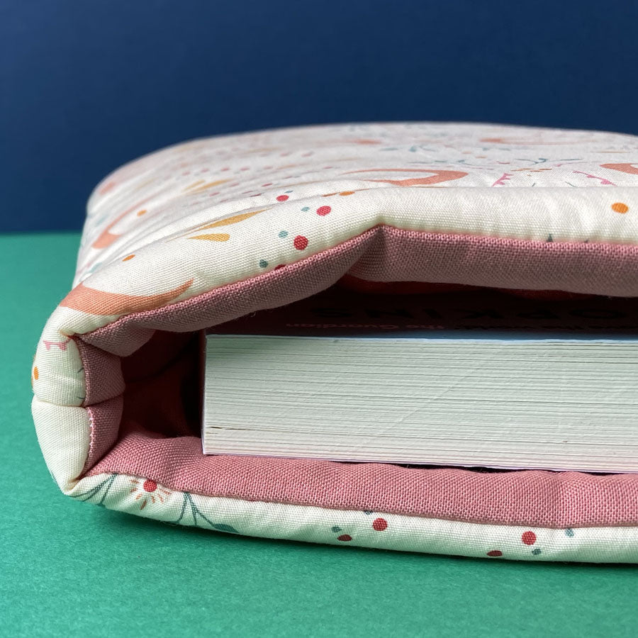 Close up of Paper and Word padded book sleeve with rose coloured fabric inside holding a fat paperback book