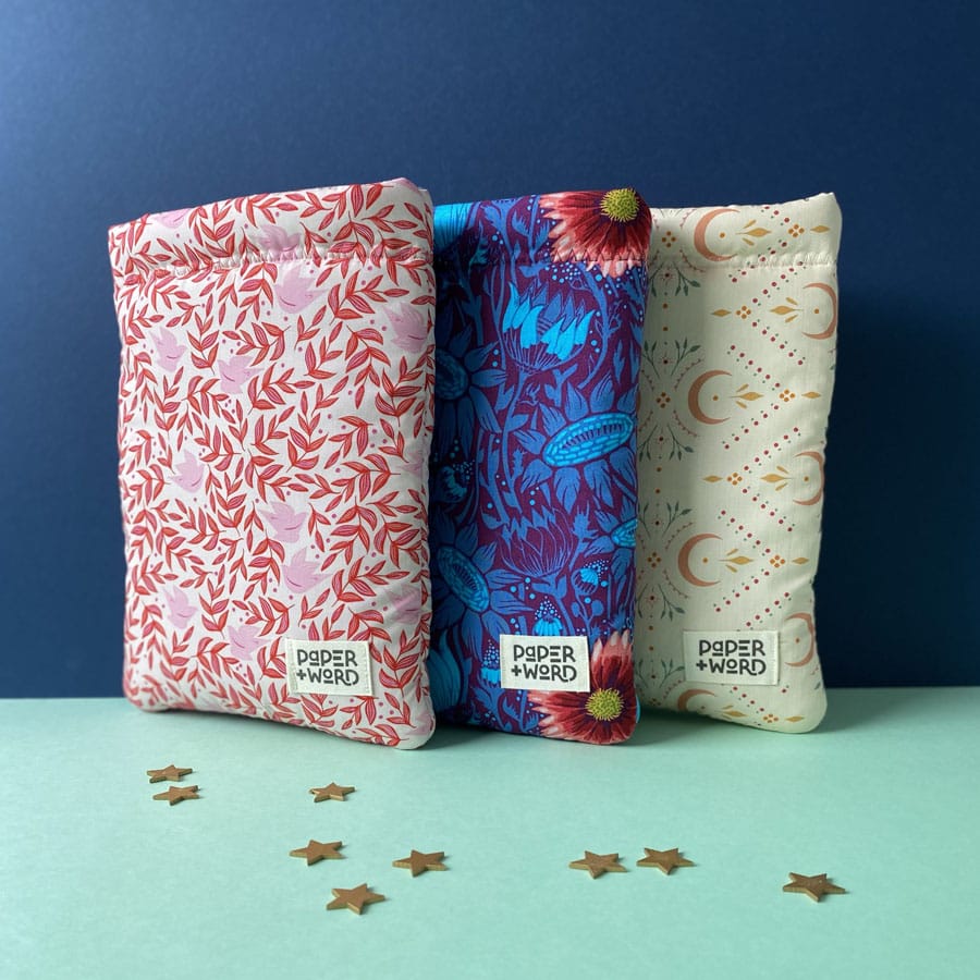 Three differently patterned padded book sleeves by Paper and Word standing upright against a dark blue background