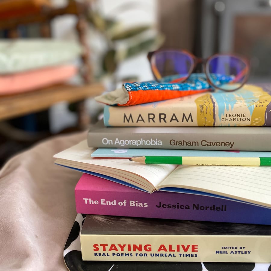 A stack of non-fiction books with glasses and a notebook