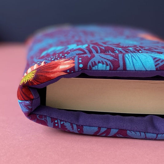 Close up detail of a dark floral patterned padded book sleeve holding a fat paperback